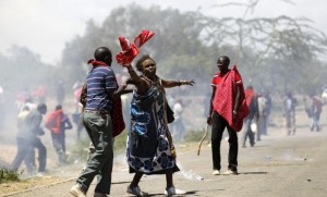 An elderly woman is assisted after riot policemen fired teargas cannisters to disperse protests to oust the Narok county Governor Samuel Tunai in Narok, Kenya