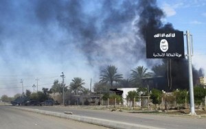 Smoke raises behind an Islamic State flag after Iraqi security forces and Shiite fighters took control of Saadiya in Diyala province from Islamist State militants, November 24, 2014. REUTERS/Stringer
