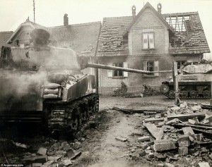 New territory: A tank moves through the ruins of a freshly retaken French town, while two medics attend to a fallen soldier on the roadside